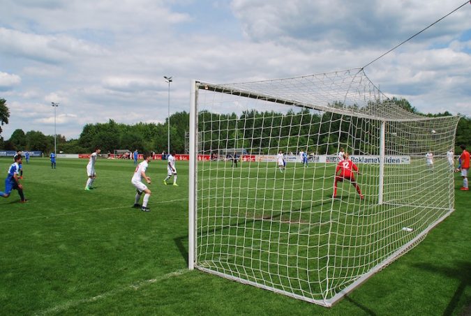 A large green field with a white football goal, with players playing football further down the field